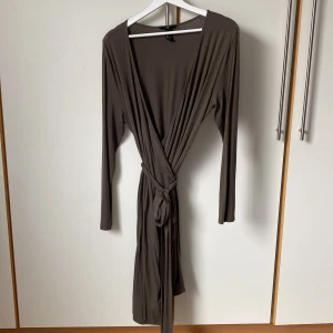 Khakigrön omlottklänning från H&M - Säljer en klassisk khakigrön omlottklänning från H&M. Klänningen är i ett tunnt följsamt material med fint fall och har hellånga ärmar och ett långt knytband i midjan. Längd 104 cm, vidden är helt justerbar. 