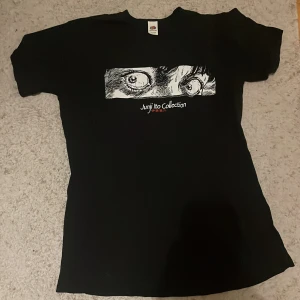 Svart t-shirt med tryck från Junji Ito Collection - Snygg svart t-shirt med ett coolt tryck från Junji Ito Collection. Perfekt för fans av skräck och manga. T-shirten har en normal passform och är kortärmad, vilket gör den bekväm att bära till vardags.