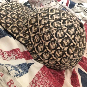 ferragamo keps med svart och beige design - Snygg farragamo keps med ett unikt mönster i svart och beige. Perfekt för att ge din outfit en cool touch. Kepsen har en justerbar rem baktill för bästa passform. Ny pris kostar 4900 kr 