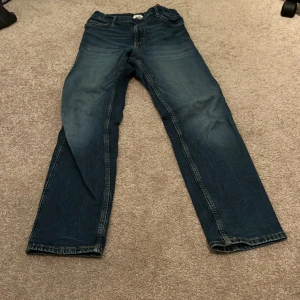Blå jeans från H&M - Snygga blå jeans från H&M med slim fit och justerbar midja. Perfekta för en avslappnad stil. Klassisk design med fem fickor och knappgylf.