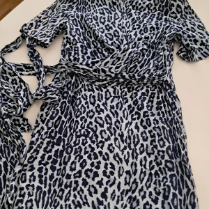 Leopardmönstrad klänning från Hans Herras - Snygg leopardmönstrad klänning från Hans Herras i blå och vit och SIDEN av högstakvalitet. Klänningen har korta ärmar och ett knytband i midjan för en smickrande passform. Perfekt för att sticka ut med stil! 🐆💙 p.s. det är 40 (FR), 36 (S) EU