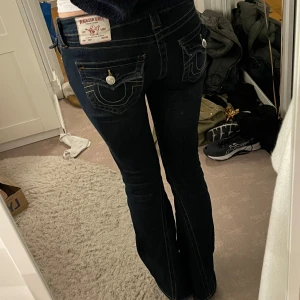 Mörkblå jeans från True Religion - Snygga mörkblå jeans från True Religion med klassiska sömmar och knappar. De har en låg midja och en bootcut-stil som ger en retro känsla. Midjemåttet är 39cm tvärsöver och innerbenslängden är 84cm ❤️❤️