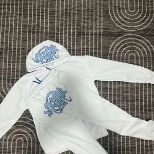 Vit hoodie med blått tryck - Säljer en stilren vit hoodie med ett coolt blått graffiti-tryck på huvan och texten 'Forgive Me' på ärmen. Hoodien har en känguruficka och blå snören vid huvan. 