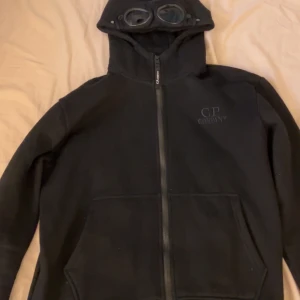 Svart tjock tröja från C.P. Company - Säljer en svart fleecejacka från C.P. Company med dragkedja och huva med inbyggda glasögon