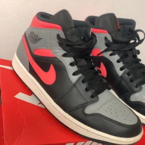 Nike Air Jordans i svart och grått med röda/rosa detaljer - Snygga Nike Air Jordans i en cool färgkombination av svart, grått och rosa. Skorna har en klassisk design med snörning och den ikoniska Air Jordan-loggan på sidan. Perfekta för dig som vill ha en stilren och sportig look. Ganska ovanligt objekt. Sjukt snygga    Köpta för 1900kr säljes för 699kr