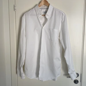 Vit skjorta från Lacoste - Klassisk vit skjorta från Lacoste med button-down krage och bröstficka. Perfekt för både formella och avslappnade tillfällen. Skjortan har långa ärmar och knappar framtill. Nyskick och i storlek 41 vilket motsvarar L. Ligger uppe en likadan i ljusblå, köps de i par säljs de för 700
