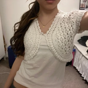 Vit virkad bolerotopp - Säljer en söt vit virkad bolerotopp med korta ärmar. Toppen har ett fint mönster och knäpps framtill med en liten pärlknapp. Strl 170 vilket jag skulle säga motsvarar strl xs/s