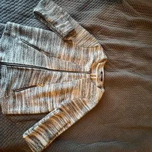 Gråmelerad jacka från Ginatex - Säljer en stilren gråmelerad jacka från Ginatex. Jackan har en dragkedja framtill och två praktiska fickor med dragkedjor. Perfekt för en avslappnad look.