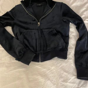Svart velourjacka från Juicy Couture - Säljer en svart velourjacka från Juicy Couture i storlek XS. Jackan har en dragkedja framtill och långa ärmar. Perfekt för en avslappnad och stilren look.