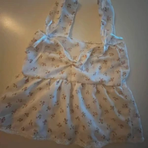 Blommig linne med spetsdetaljer - Charmig vit linne med små blommor i olika färger. Toppen har knytband vid axlarna och spetsdetaljer vid nederkanten. Perfekt för en somrig look. Egen sydd och väldigt fin i storlek s/xs