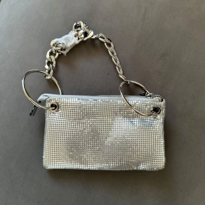 Liten väska - Liten silvrig väska från Asos med litet innerfack för kort eller liknande. Ny, aldrig använd, kommer i det skick den är köpt. (Tre sista bilderna är lånade från Asos där väskan är köpt från).