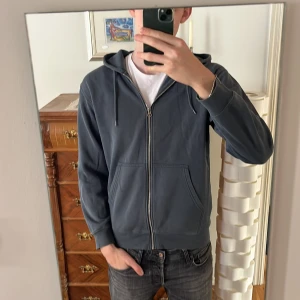 Mörkgrå hoodie från Weekday - Säljer en stilren mörkgrå hoodie från Weekday. Den har en dragkedja framtill och en praktisk huva med snörning. Perfekt för en avslappnad look. Två fickor framtill för extra bekvämlighet. Jag är 194 cm och den är lite liten så om man har storlek M så passar den 