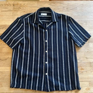 Randig kortärmad skjorta från Zara - Snygg randig skjorta från Zara i mörkblått och vitt. Skjortan har korta ärmar och knappar framtill. Perfekt för en stilren look. Fortfarande nyskick, bara använd några få gånger 