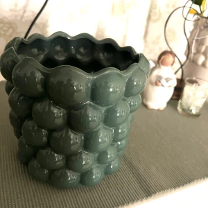 Grön bubblig kruka - Säljer en unik grön kruka med bubblig design. Krukan har en glansig yta och en vågig kant upptill. Perfekt för att ge ditt hem en modern och lekfull touch. Passar utmärkt för  växter eller som en dekorativ detalj.