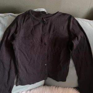 Svart ribbad kofta - Säljer en svart ribbad kofta med knappar framtill. Koftan har långa ärmar och en enkel design som passar till många tillfällen. Perfekt för lager-på-lager-stil.