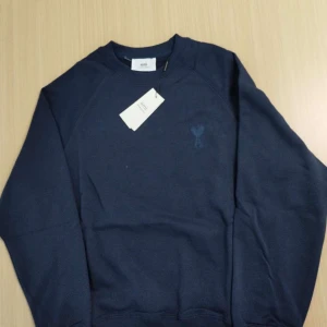 Mörkblå sweatshirt från Ami - Säljer en stilren mörkblå sweatshirt från Ami med ett diskret hjärtdetalj på bröstet. Tröjan har en klassisk rund halsringning och långa ärmar. Perfekt för en avslappnad look.