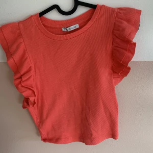 Korallfärgad topp med volangärmar från Zara - Säljer en söt korallfärgad topp från Zara med volang på ärmarna. Toppen är ribbad och är perfekt nu till sommaren! Skriv till mig innan ni trycker på köp nu! Köparen står för frakt✨