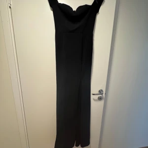 Svart långklänning från Nelly - Elegant svart långklänning från New Eve med offshoulder-design och dragkedja i ryggen💃 Perfekt för en stilren look🪩 En slits på högerben🖤 Använd 1 gång!!