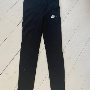 Svarta träningstajts från Nike - Snygga svarta träningstajts från Nike med deras ikoniska logga på benet. Perfekta för både träning och vardag. De är tillverkade i ett mjukt och stretchigt material.