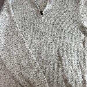 Grå stickad tröja från Chaps - Säljer en stilren grå stickad tröja från Chaps med dragkedja vid halsen. Perfekt för kyligare dagar med sin mjuka och bekväma passform. Tröjan har långa ärmar och en diskret melerad design.