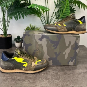 Valentino Rockrunner Intressekoll - Snygga Valentino Rockrunner sneakers med en unik kombination av grönt, brunt och neon gult i ett kamouflagemönster. Skorna har en klassisk snörning och är tillverkade i en mix av mocka och skinn. Perfekta för att ge din outfit en cool touch. Endast Intressekoll och box och dustbag medkommer!