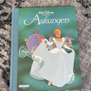 Askungen - Säljer en klassisk barnbok från Walt Disney, 'Askungen'. Boken har en vacker illustration av Askungen i sin blå klänning på omslaget och innehåller originalillustrationer som tar dig till ett magiskt land. Perfekt för alla som älskar sagor och Disney.26x21cm