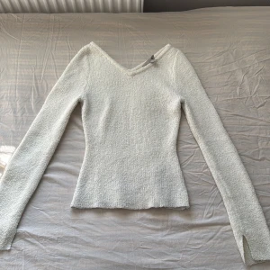 Vit stickad tröja med v-ringning - Säljer en stilren vit stickad tröja med v-ringning. Tröjan har långa ärmar med slits och en mjuk textur som ger en bekväm känsla. Perfekt för kyligare dagar!