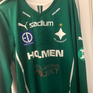 IFK Norrköping matchtröjor signerade - Två långärmade IFK Norrköping fotbollströjor från Puma, en grön och en röd, båda med tryckta sponsorer och klubbmärke. Båda tröjorna är signerade av spelare och har stora siffror på ryggen (91 och 10). Perfekt för samlare eller fans! 