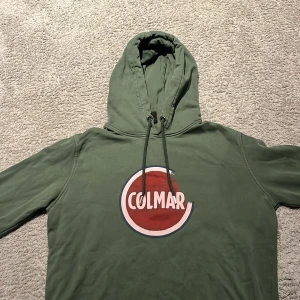 Grön hoodie från Colmar - Säljer en grön hoodie från Colmar med stor logga framtill (slitningarna är menade). Tröjan har huva och är tillverkad i mjukt material. Nypris ca 2000. Perfekt för en avslappnad stil.
