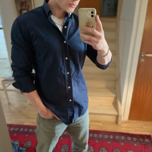 Mörkblå skjorta från Ralph Lauren - Säljer en klassisk mörkblå skjorta från Ralph Lauren i modellen Custom Fit. Skjortan har knappar framtill och en stilren krage. Perfekt för dig som gillar en tidlös och snygg look.