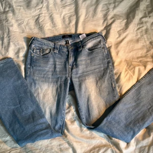 Ljusblå jeans från True Religion - Säljer ett par ljusblå jeans från True Religion med klassiska kontrastsömmar och detaljerade fickor med knappstängning. Det är storlek w27, Jeansen har en rak passform och är tillverkade i denim. Perfekta för dig som gillar en ikonisk och avslappnad jeansstil!💖💅😍🌊
