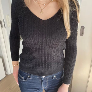 Svart kabelstickad tröja från Massimo Dutti - Säljer denna supergulliga svarta kabelstickade tröjan från Massimo Dutti med v-ringning och lång ärm. Den har ganska tight passform, vilket är snyggt. Perfekt till jeans eller kjol nu på våren💕