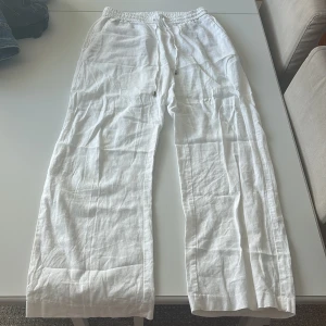 Vita linnebyxor med resår och dragsko - Säljer ett par vita linnebyxor med resår i midjan och justerbar dragsko. Byxorna har raka, vida ben och en bakficka. Perfekta för varma dagar och en avslappnad stil.