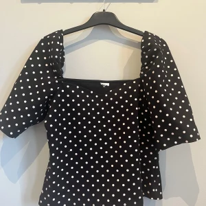 Svart prickig blus med puffärmar - Säljer en svart blus med vita prickar och puffiga korta ärmar. Blusen har en v-ringad halsringning och figurnära passform. 