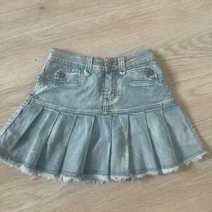 Jeanskjol med volang och fransad kant - Säljer en ljusblå jeanskjol med volang nedtill och fransad kant. Kjolen har fickor fram och bak samt bälteshällor och knappstängning. Perfekt för en cool och avslappnad stil.