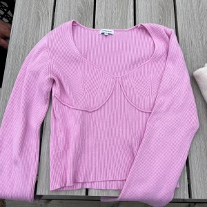 Rosa ribbad tröja från Bubble Room - Säljer en ljusrosa ribbad tröja från Bubble Room med markerade sömmar över bysten och v-ringad hals. Tröjan har långa ärmar och är figurnära i modellen. Perfekt för dig som gillar trendiga och feminina plagg!