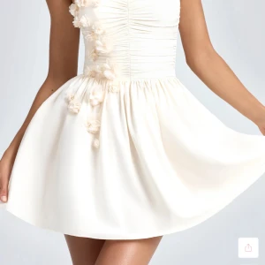 Vit axelbandslös kortklänning med blommor - En romantisk och feminin klänning med vackra blommiga applikationer och korsettdesign. Den korta, utsvängda klänningen och snörningen i ryggen skapar en elegant och smickrande passform. perfekt för festliga tillfällen eller bara en fin sommarklänning. Den är i storlek XS-S. Den är helt ny och taggarna sitter fortfarande på.