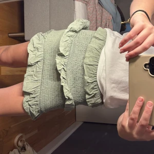 Grön volangkjol med smock - Säljer en ljusgrön kort kjol med smock och volangdetaljer. Kjolen har en elastisk midja och två volanger som ger en söt och trendig look. Perfekt att matcha med en enkel topp för en avslappnad stil.