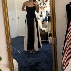 Svart och vit långklänning - Säljer en elegant svart långklänning med vita paneler. Klänningen har smala axelband och figurnära passform upptill. Perfekt för speciella tillfällen när du vill sticka ut. Väldigt stretchig så skulle passa från S-L