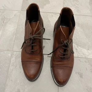 Bruna skinnboots från GH George Hogg - Snygga bruna boots i skinn från GH med snörning framtill och elastiska paneler på sidorna. Skorna har rund tå och låg klack, perfekt till vardagsstilen. Klassisk design med svarta detaljer vid sulan.