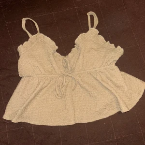 Ett beige linne med fina detaljer - Ett beige linne med knut på framsidan och urringning där fram