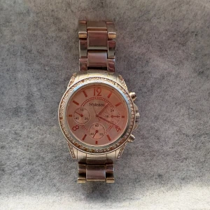 Klocka från Styleicon - Säljer en snygg klocka från Styleicon med glittriga stenar runt urtavlan. Klockan har en metall-länk och roséguldfärgad urtavla med flera små urtavlor. Perfekt accessoar för att lyfta din outfit.