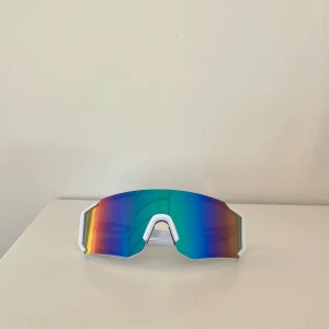 Vita sportiga solglasögon - Snygga sportglasögon med vit båge och stora spegelglas i blått, grönt och lila. Glasögonen har en modern, kantig form och passar perfekt för träning utomhus☀️ Lätta och bekväma att bära😎