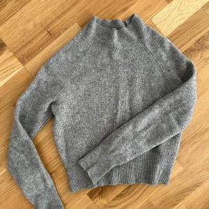 Grå stickad polotröja från HM - Säljer en grå stickad cashmere polotröja från H&M i mjukt material. Tröjan har lång ärm, ribbad struktur och hög krage. Perfekt för lager-på-lager och enkel att matcha med olika outfits. Storlek S men känns mer som en XS. 