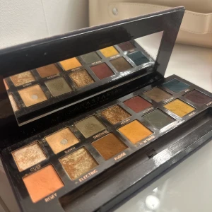 Subculture ögonskuggspalett från Anastasia Beverly Hills - Pris kan diskuteras! En ögonskuggspalett med 14 nyanser i både matta och skimrande färger. Paletten innehåller bland annat guld, olivgrönt, senapsgult, blått och vinrött. Kommer i en mörkgrå förpackning med spegel inuti.