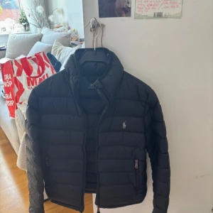  Ralph Lauren jacka - Säljer en svart dunjacka från Polo Ralph Lauren i storlek XS. Jackan har klassisk pufferdesign, dragkedja framtill och den ikoniska loggan broderad på bröstet. Perfekt för kyligare dagar och enkel att matcha med olika outfits.