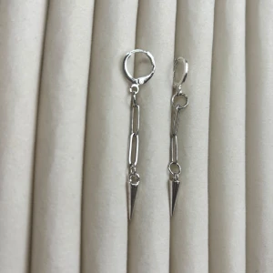 Silverfärgade örhängen med kedja och spetsig detalj - Säljer ett par trendiga silverfärgade örhängen med kedjelänkar och en spetsig konformad detalj längst ner. Perfekta för dig som gillar en edgy och modern stil.