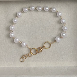 Pärlarmband med guldfärgade detaljer - Stilrent armband med vita pärlor och guldfärgade länkar. Justerbar längd med flera ringar och karbinlås. Perfekt accessoar för att lyfta din outfit.