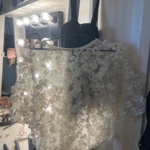 Vit blus med volangdetaljer från Gina Tricot - Superfin vit blus från Gina Tricot med massor av volangdetaljer som ger en fluffig och unik look. Blusen är genomskinlig och har korta ärmar. Perfekt för dig som vill sticka ut med en cool och trendig topp!