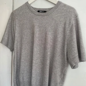 Grå stickad kortärmad tröja från Gina Tricot - Säljer en enkel och stilren grå stickad tröja från Gina Tricot. Tröjan har korta ärmar, rund halsringning och är perfekt för lager-på-lager. Passar till många olika outfits!